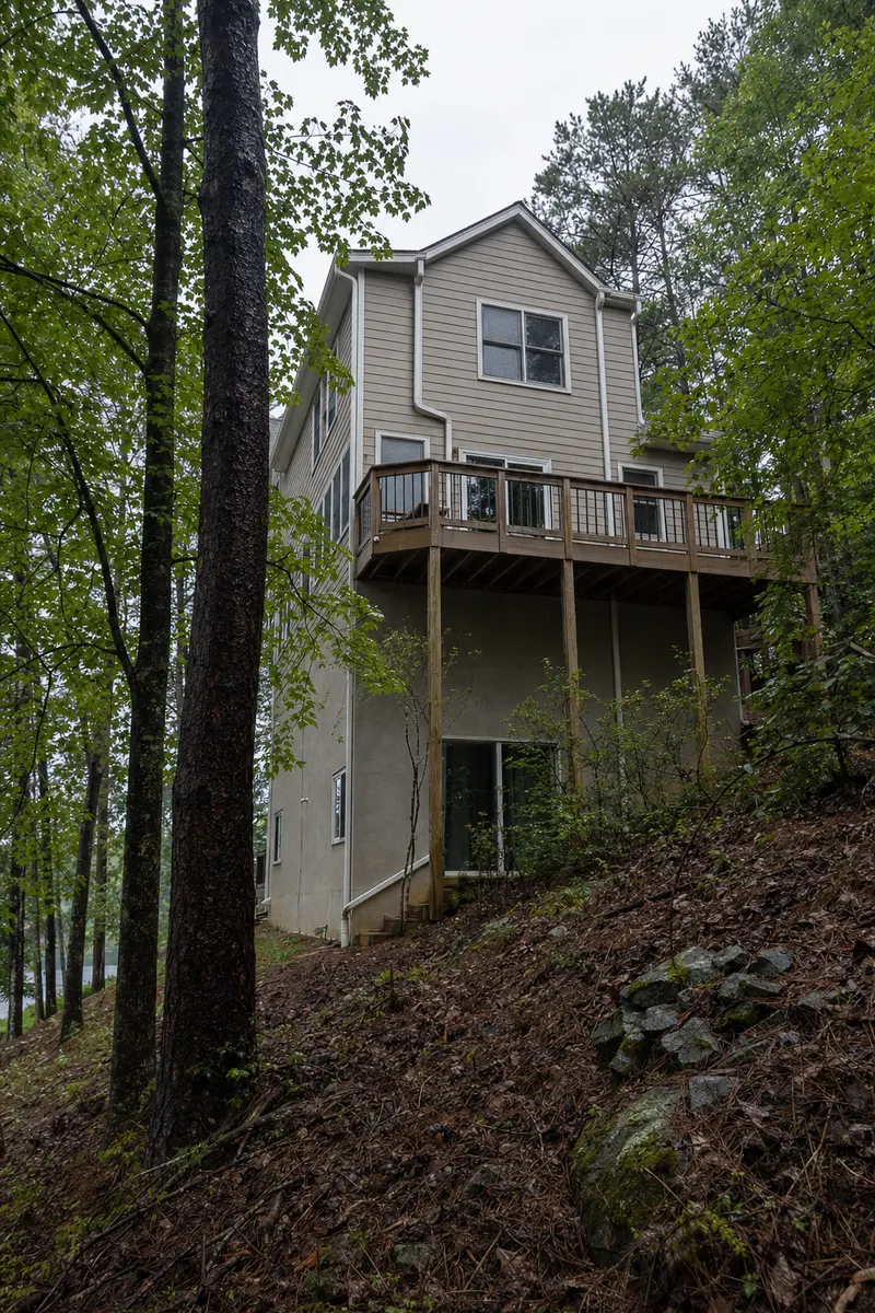 The downhill side of a lake house, three levels tall, with gutters and downspouts above a steep wooded lot